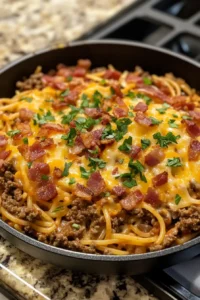  A skillet filled with cowboy spaghetti, generously topped with melted cheese, crispy bacon pieces, and chopped parsley.