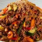 A plate of Mongolian ground beef with colorful bell peppers, onions, and zucchini, garnished with sesame seeds.