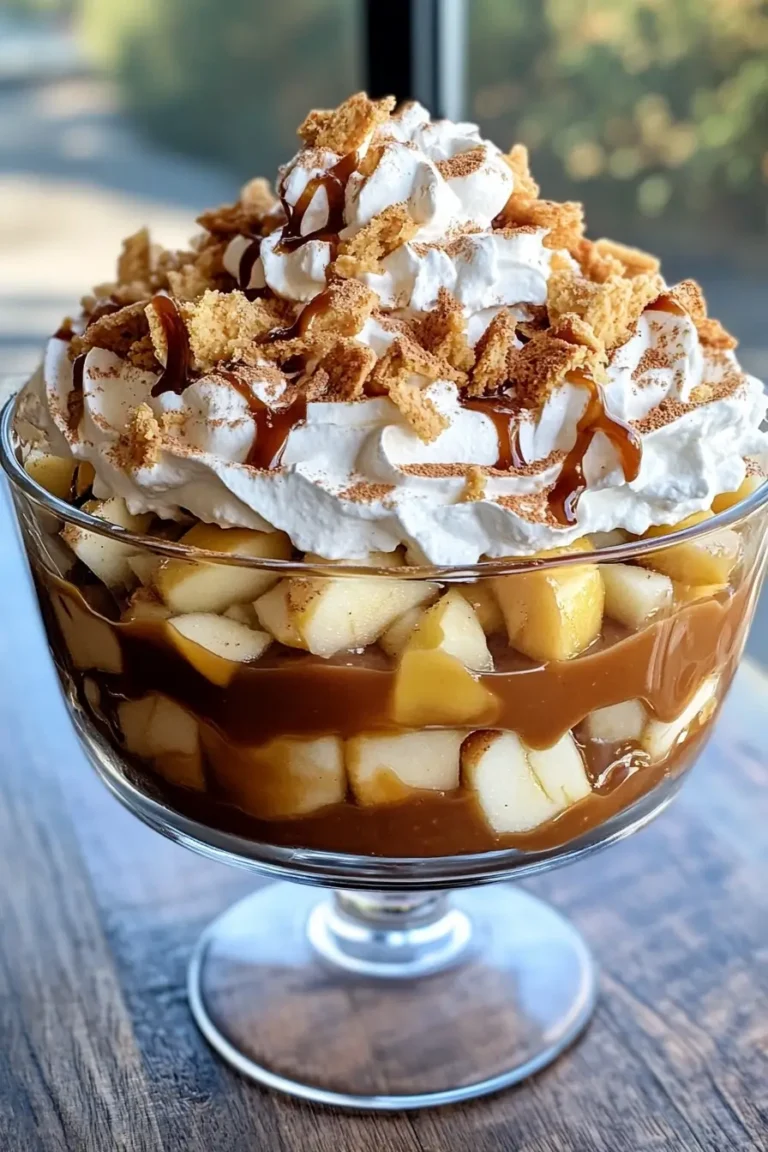 A caramel apple trifle layered with diced apples, caramel sauce, whipped cream, and crumbled cookies in a glass trifle dish.