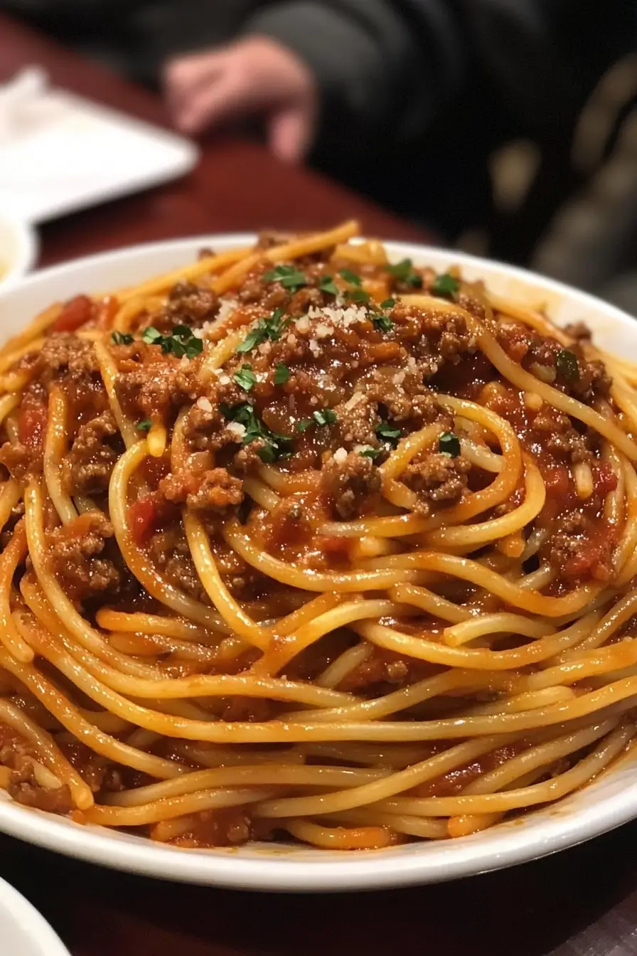 A close-up of a plate of spaghetti Bolognese, featuring al dente pasta topped with a rich, meaty tomato sauce, garnished with freshly grated Parmesan cheese and chopped parsley.
