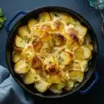 A casserole dish of Creamy Au Gratin Potatoes on a dark surface, topped with a golden crust and garnished with herbs.