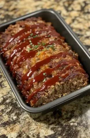 A freshly baked classic meatloaf topped with a glossy ketchup glaze, garnished with parsley, served in a loaf pan on a granite countertop.