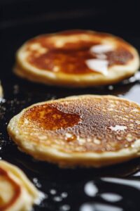  Fluffy Lemon Ricotta Pancakes cooking on a hot skillet, golden brown and glistening with melted butter.