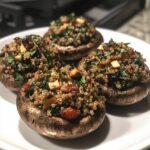 Four Stuffed Portobello Mushrooms filled with a mixture of quinoa, spinach, sun-dried tomatoes, and herbs, served on a white plate.