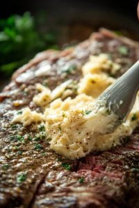 Close-up of smoked rib being brushed with garlic butter and garnished with fresh herbs.