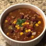 A bowl of taco soup with ground meat, kidney beans, corn, diced tomatoes, and topped with a sprig of fresh cilantro.