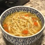 A bowl of homemade chicken noodle soup with shredded chicken, noodles, carrots, and broth, served in a decorative ceramic bowl.