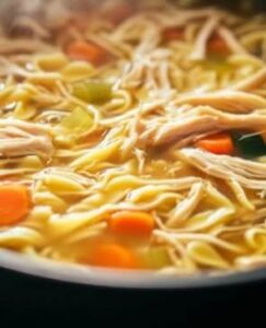  A pot of chicken noodle soup simmering with shredded chicken, egg noodles, carrots, celery, and a flavorful broth