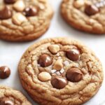 Close-up of freshly baked peanut butter cookies topped with chocolate chips and peanut butter chips, sprinkled with sea salt.