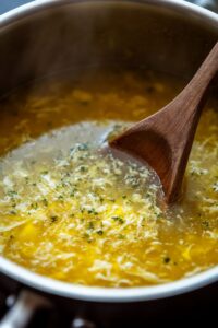  A pot of freshly made egg drop soup with herbs, stirred with a wooden spoon.Title: Freshly Prepared Egg Drop Soup