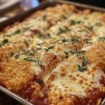 A freshly baked tray of chicken Parmesan topped with melted cheese, tomato sauce, breadcrumbs, and garnished with fresh basil.