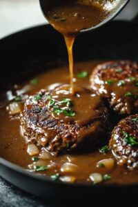 Juicy Salisbury steak patties in a skillet, smothered with rich brown gravy being poured over them, garnished with fresh parsley.