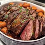 Sliced chuck roast served in a dish with tender carrots, garnished with fresh herbs and a savory sauce.