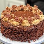 A beautifully decorated German chocolate cake with rich chocolate frosting, piped cream swirls, and topped with pecans and chopped nuts