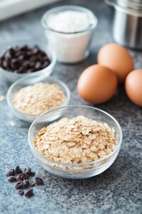 Ingredients for oatmeal cookies, including oats, chocolate chips, eggs, flour, and sugar, arranged on a countertop.