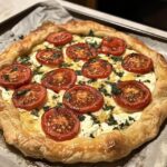 A freshly baked Tomato Ricotta Galette with golden puff pastry, creamy ricotta filling, and vibrant tomato slices garnished with fresh herbs.