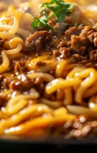 A steaming hot skillet of Mongolian ground beef noodles, coated in a rich, savory sauce and garnished with fresh herbs.