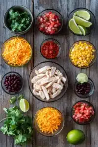 A rustic wooden table with neatly arranged bowls of shredded chicken, black beans, corn, shredded cheese, fresh cilantro, pico de gallo, lime wedges, and spicy salsa, showcasing vibrant ingredients for a Chicken Taco Dump.