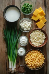 A rustic wooden table displays various ingredients for Mac and Cheese Cowboy Cups, including elbow macaroni, shredded and sliced cheese, green onions, cottage cheese, sour cream, milk, and seasonings.