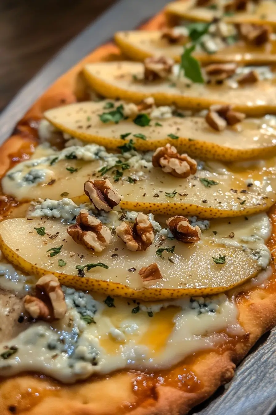 Close-up of a flatbread topped with sliced pears, crumbled blue cheese, chopped walnuts, and fresh herbs.